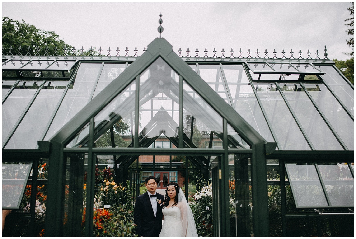 bride and groom standing under a greenhouse
