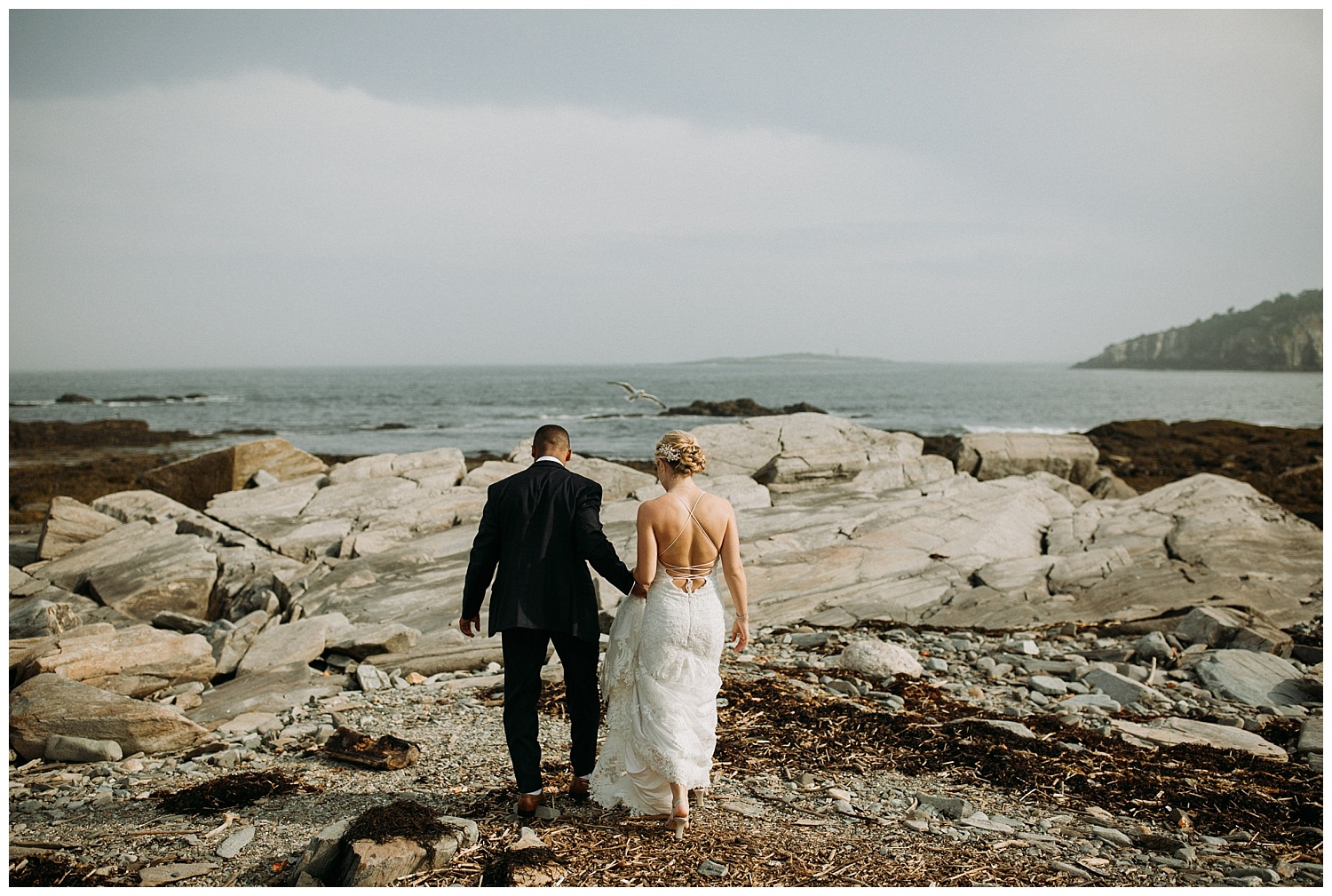 a bride and groom walking on a maine beach