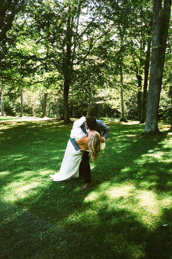 A groom dips a bride in the forest in Vermont
