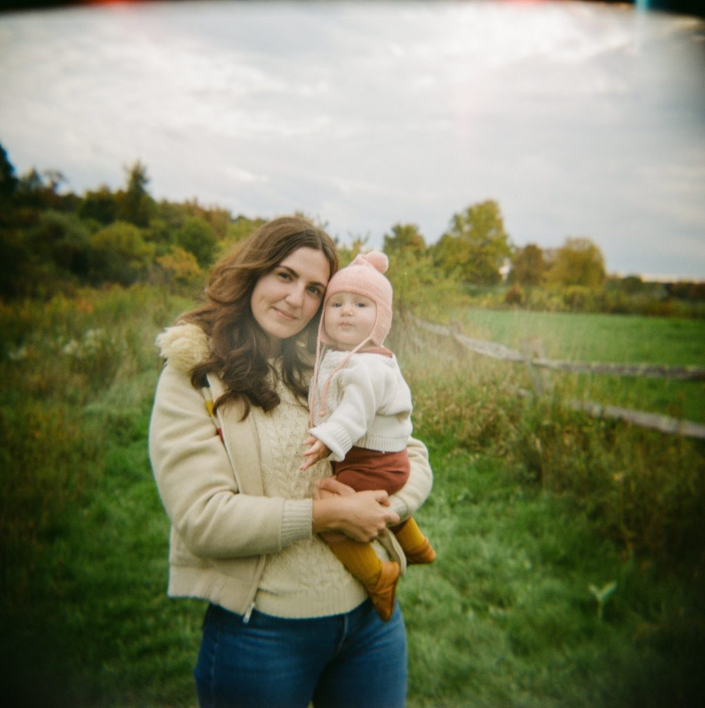 a mother holds her daughter in a field and looks into the camera