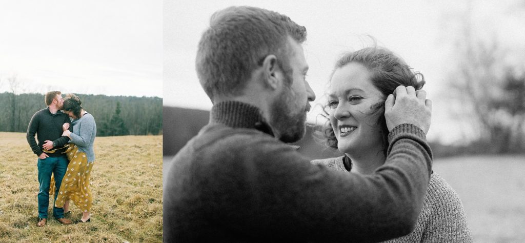Outdoor couple embraces next to a man brushing the windswept hair out of his fiancée's face 