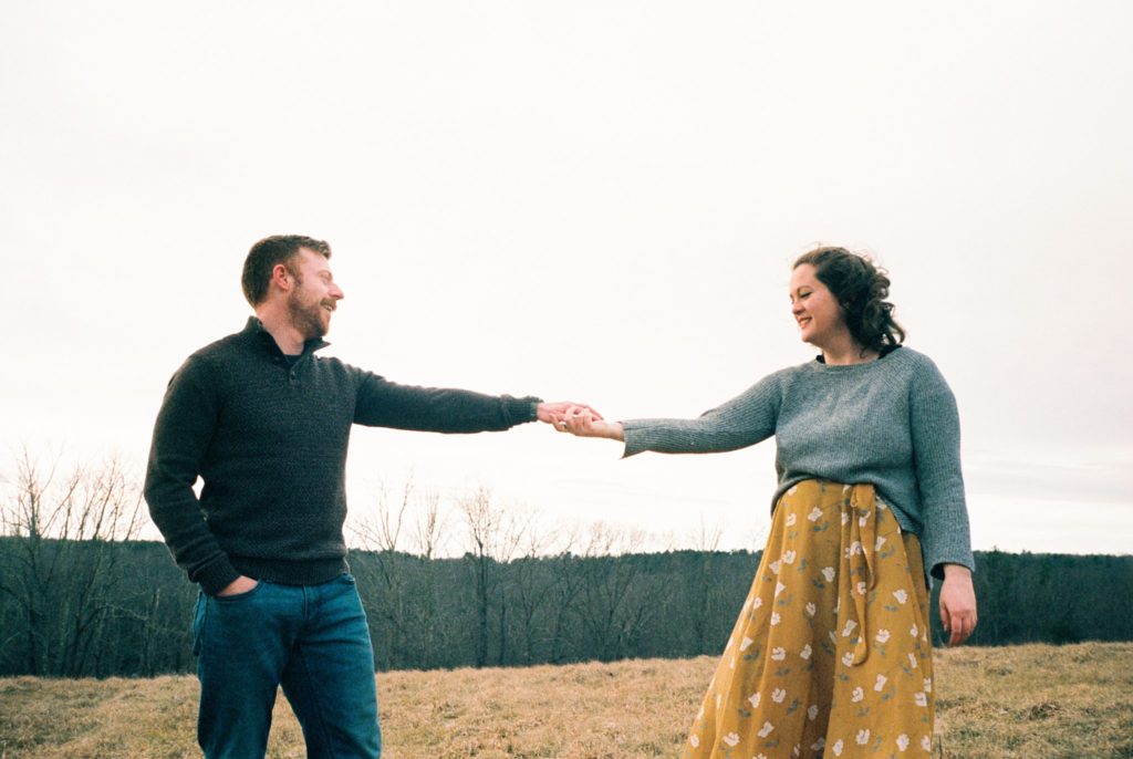 Engaged New England man holds the hand of his fiancée near a forest