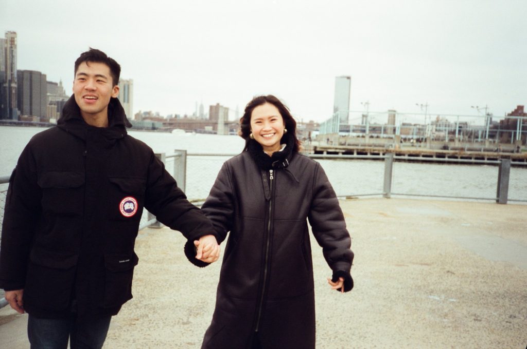 Couple with clasped hands smiles along Brooklyn waterfront