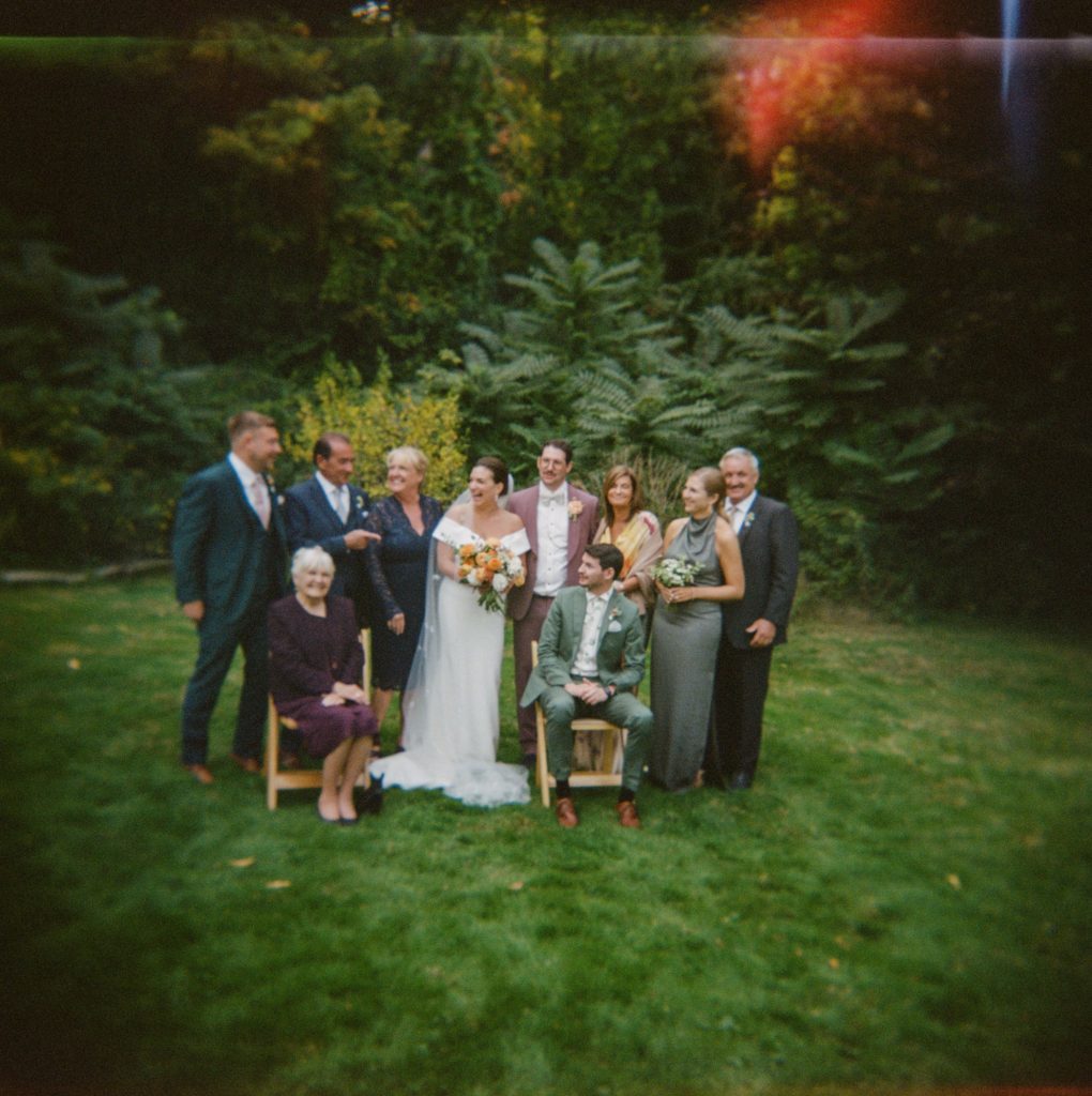 Film photo of bride and groom with their families in a back yard