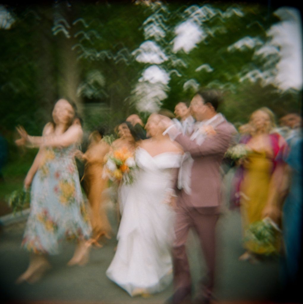 Motion blur film photo of bride, groom and wedding party walking after backyard wedding ceremony