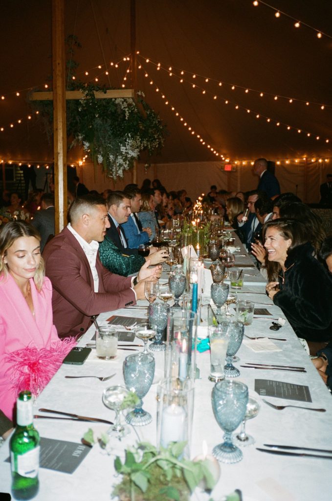 Wedding guests laugh and celebrate while seated at banquet table inside reception space, captured on film