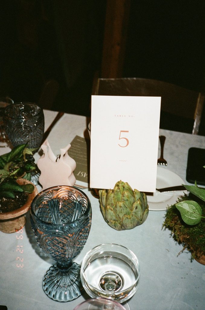Film photo of modern wedding details including table number and unique glasses