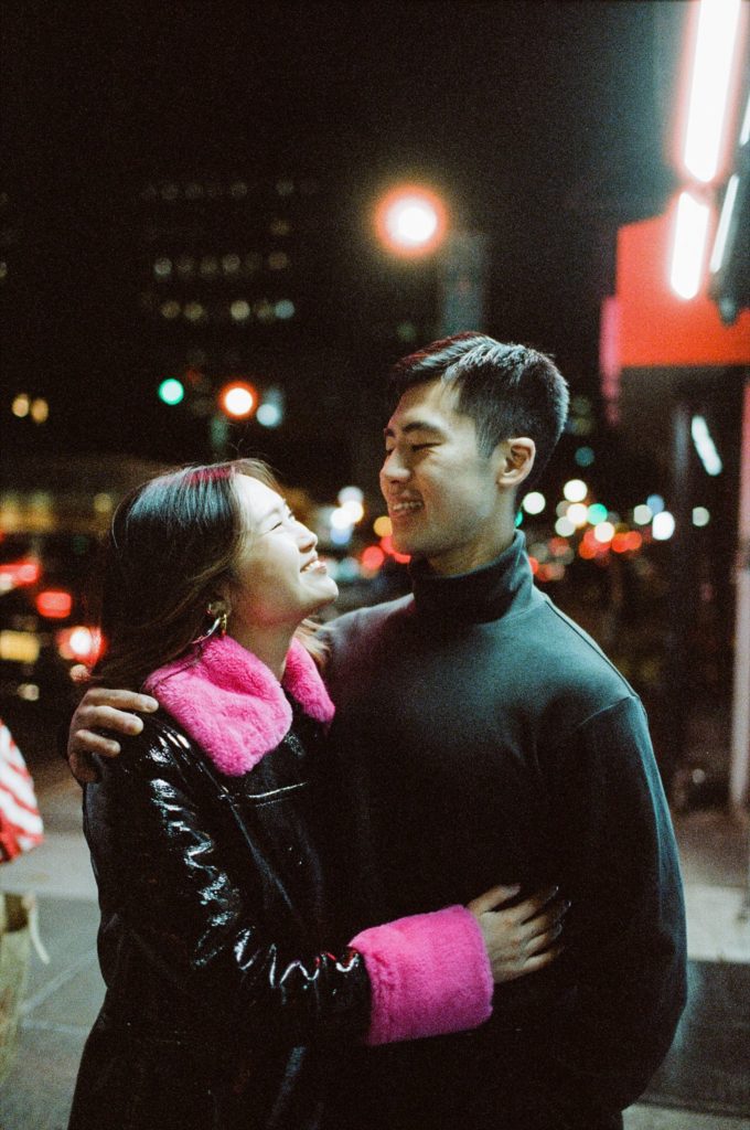 NYC couple smiles at each other, embracing on the streets of New York