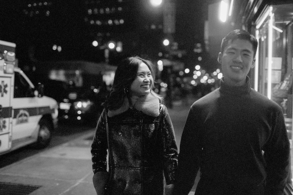 Black and white film photo of smiling couple walking down the city street