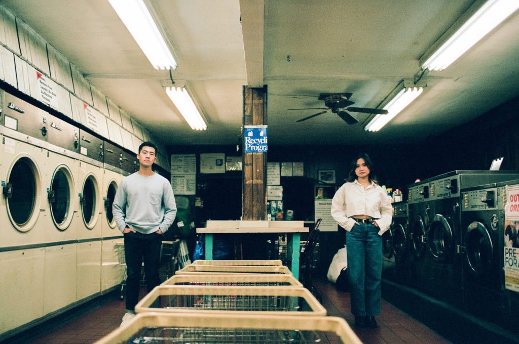 Film photograph of man and woman symmetrically standing on opposite sides of a laundromat aisle 