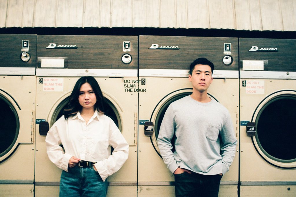 Film portrait of engaged couple dramatically posed in front of laundry machines