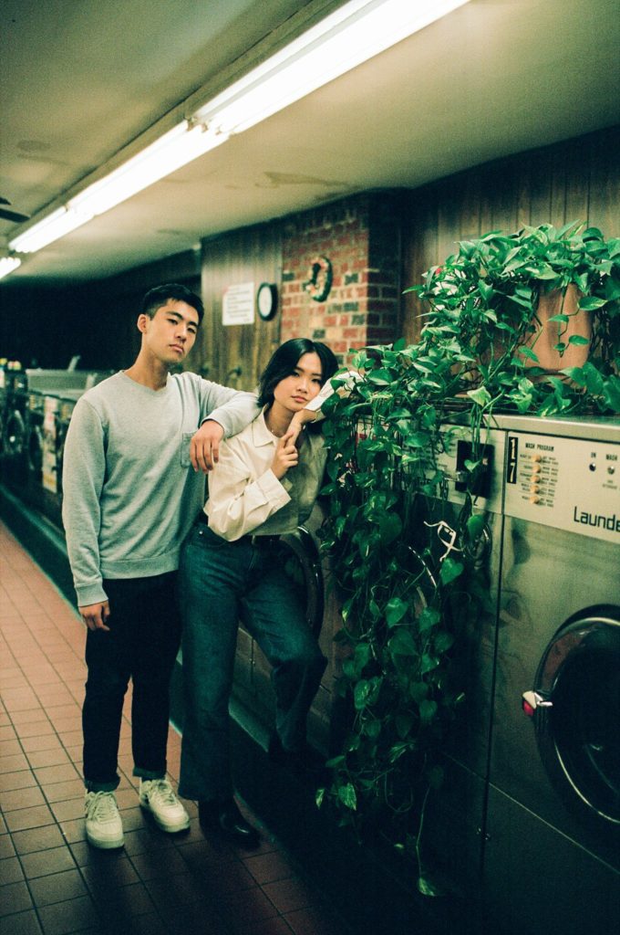 Couple stands among washing machines and houseplants in vintage NY laundromat
