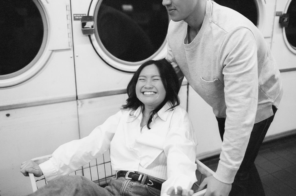 Black and white film photo of woman laughing while she is pushed in a cart by her love