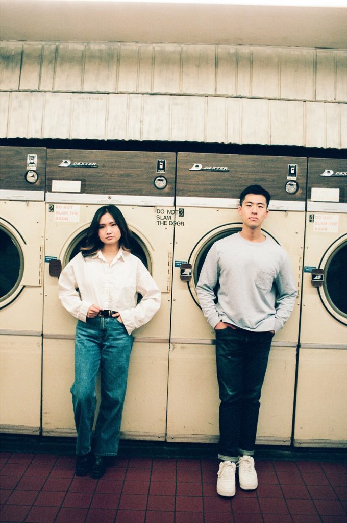 Engaged man and woman stand side by side in front of vintage washing machines