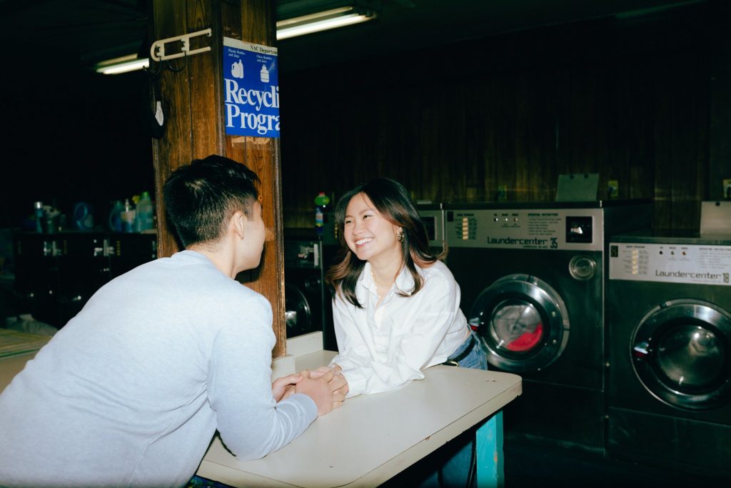 Smiling couple clasps hands over a table in Brooklyn laundromat