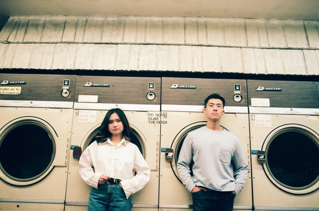 Side by side portrait of man and woman in front of vintage washing machines in Brooklyn
