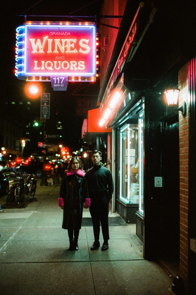Brooklyn couple holds hands on the street at night with neon lights above