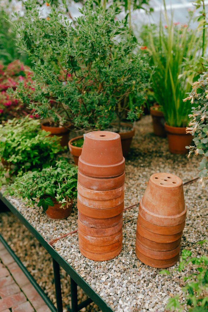 Stacked terra cotta pots inside a greenhouse among plants