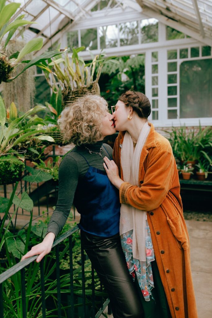 Engaged couple kisses passionately set against overflowing plants and vegetation, captured on film