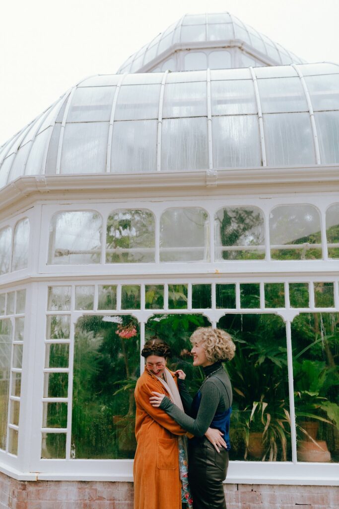 Boston couple laughs together outside of a greenhouse window