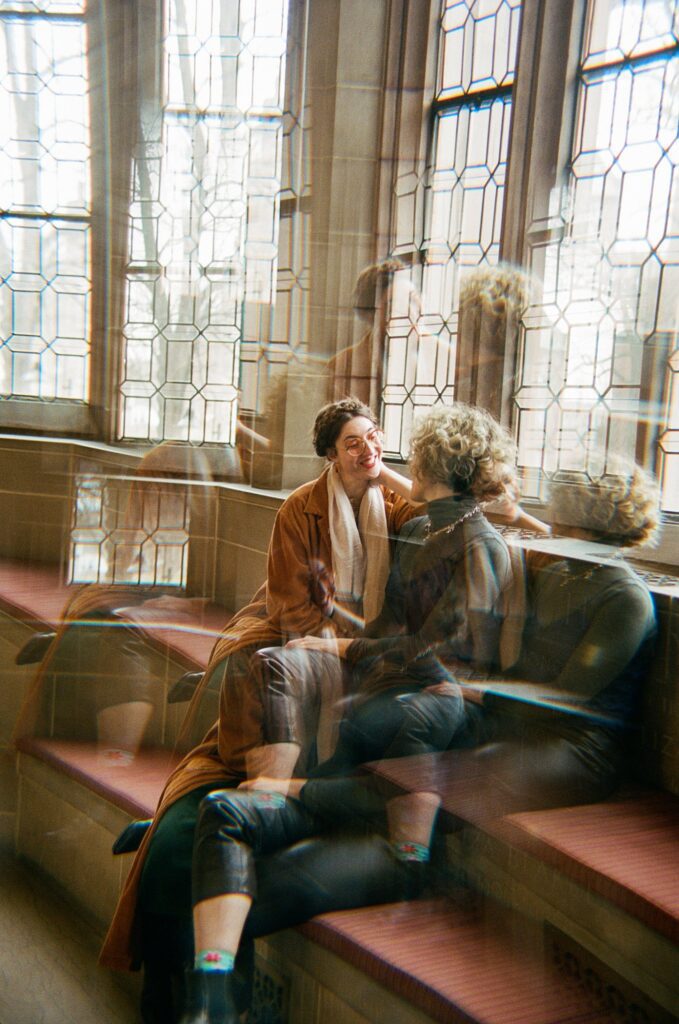 Film portrait of engaged couple sitting beneath large windows as seen through a prism