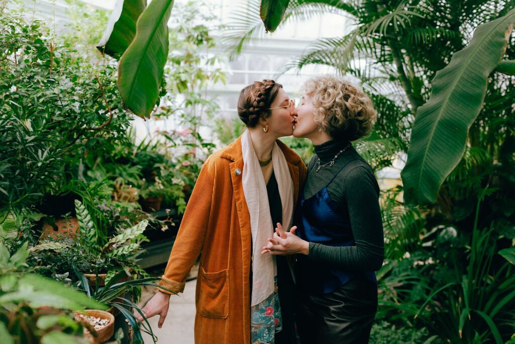 35mm photo of same sex couple kissing surrounded by dense and varied foliage in a greenhouse