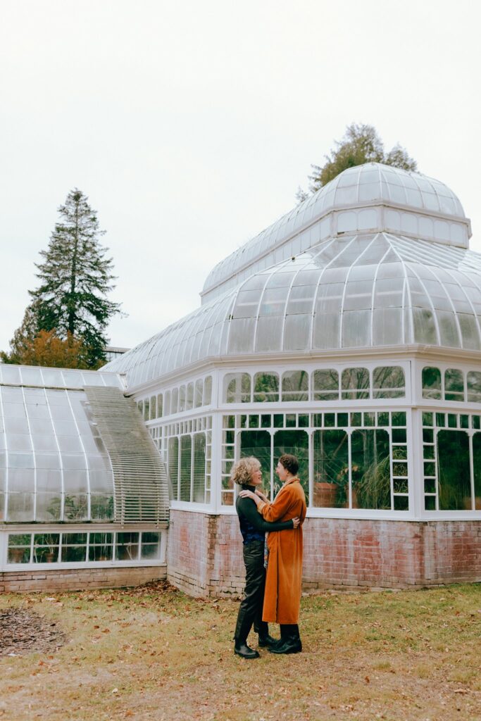 Boston couple embraces outside of a greenhouse, captured on film
