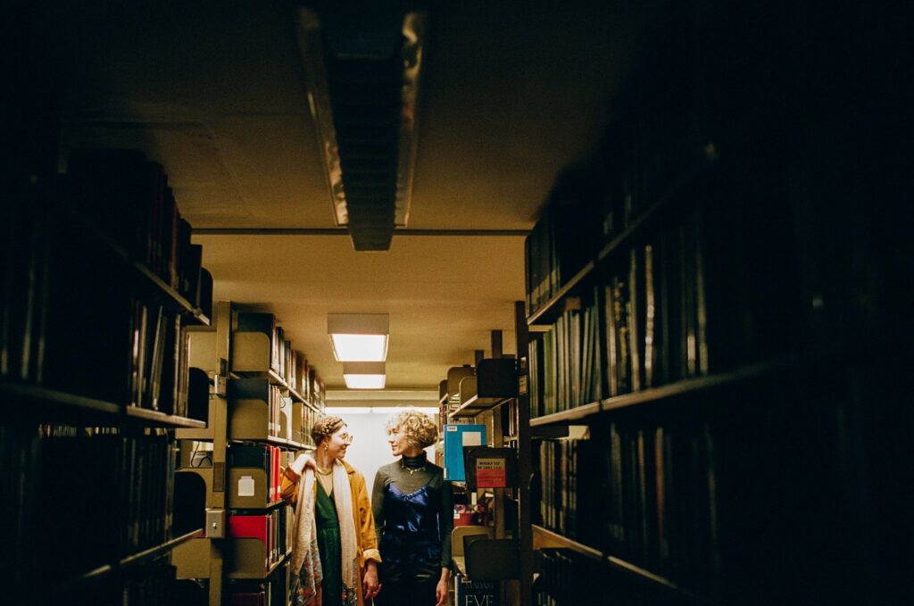 Film portrait of engaged couple standing together among shelves of books