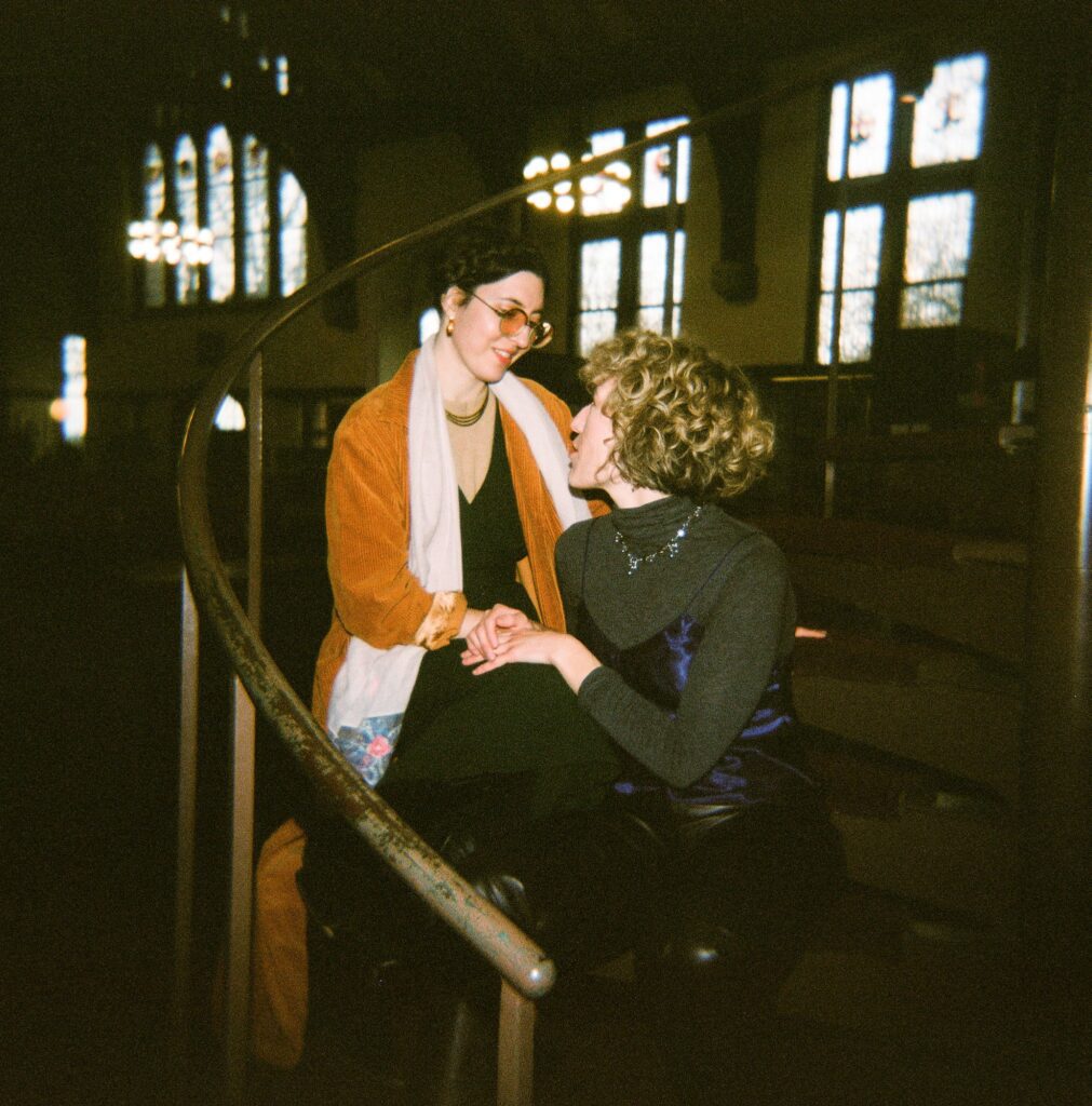 Same sex couple sits together inside a library, captured on film