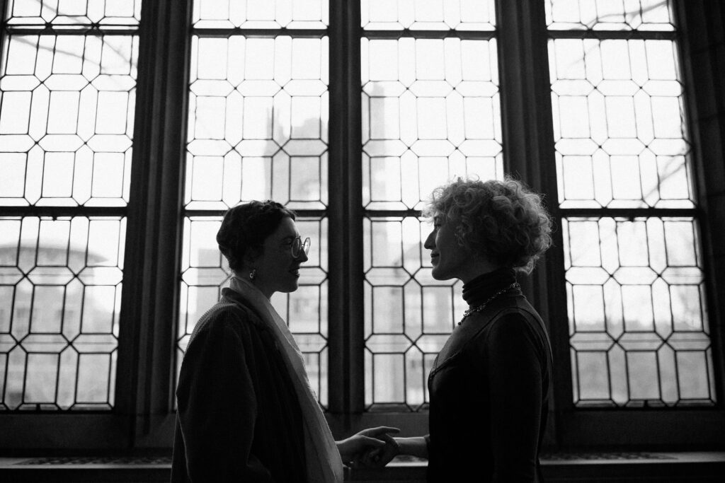 Black and white film photo of couple silhouetted against large windows