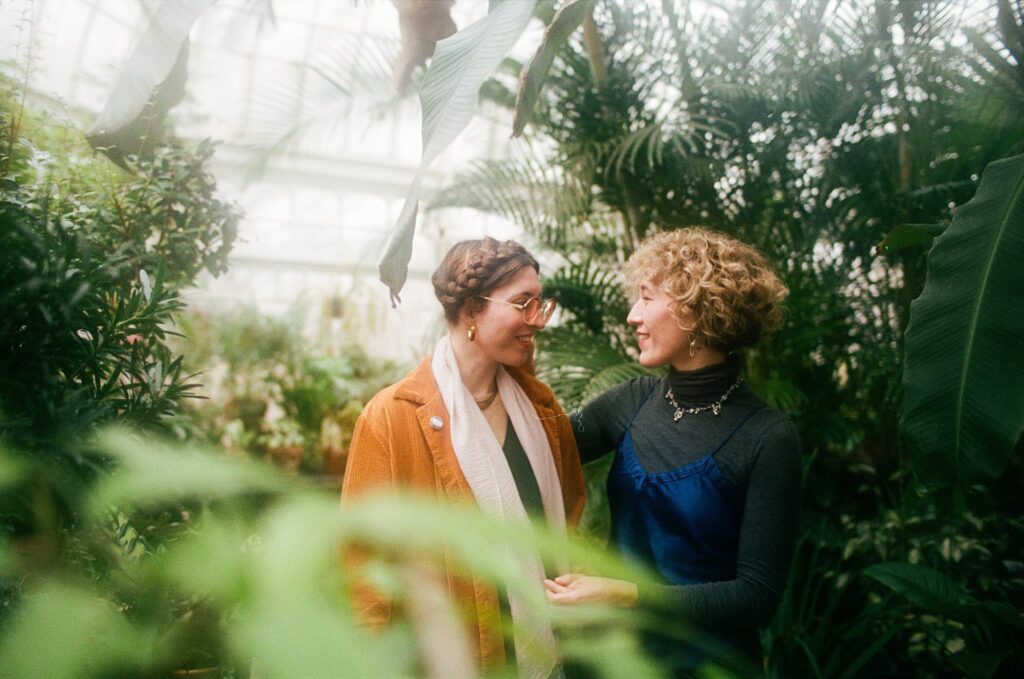Film portrait of engaged couple looking at each other while surrounded by greenery