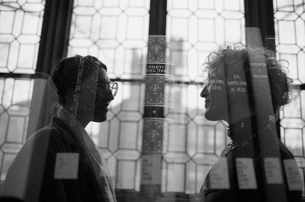 Double exposure black and white film photograph of a silhouette of a couple in front of a large window against library books 