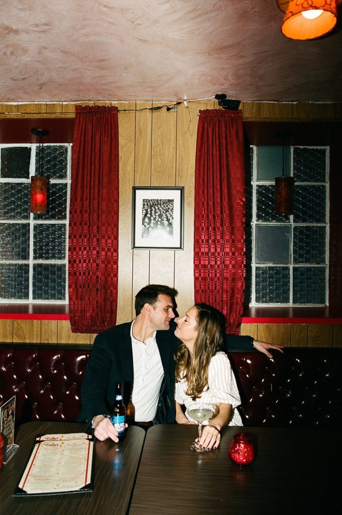 Engaged man and woman lean in for a kiss in a vintage Boston bar illuminated by direct flash
