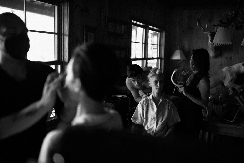 Black and white film photo of brides getting ready for wedding surrounded by friends