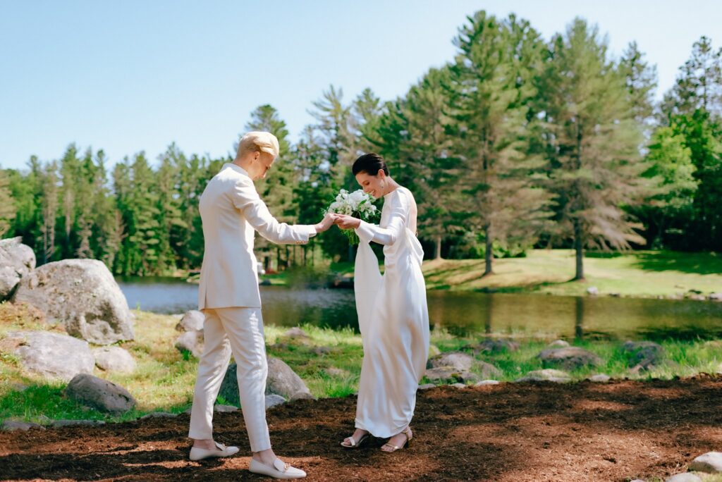 Two women hold hands in their wedding attire at upstate Adirondack estate