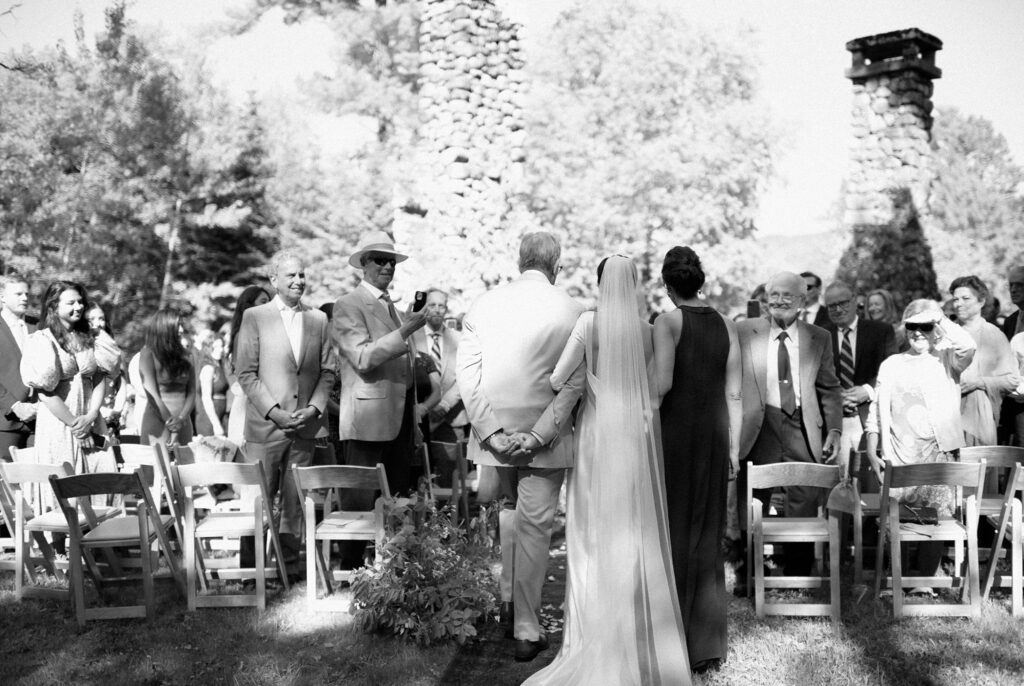 Black and white film photograph of bride walking down the aisle