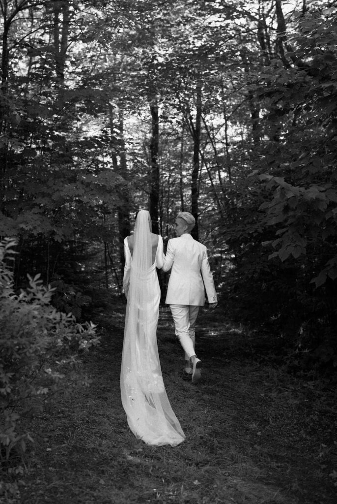 Two brides walk together into the Adirondack forest, captured on film in black and white
