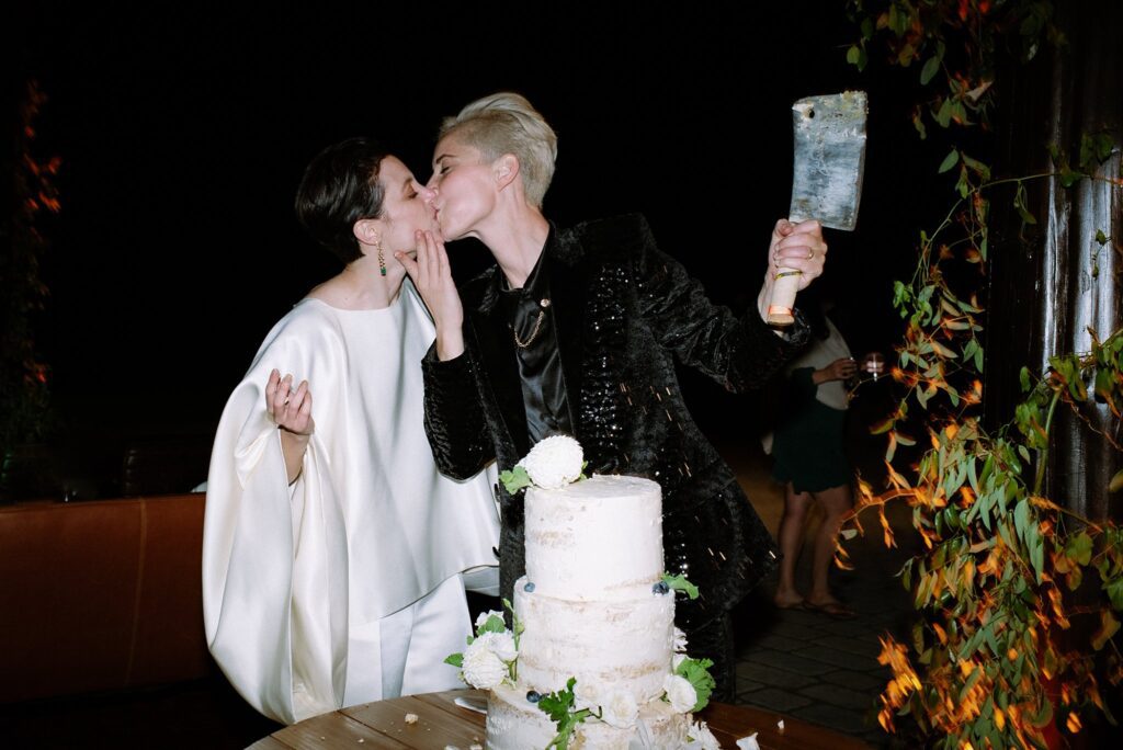 Brides kiss after cutting the cake at luxury upstate New York wedding