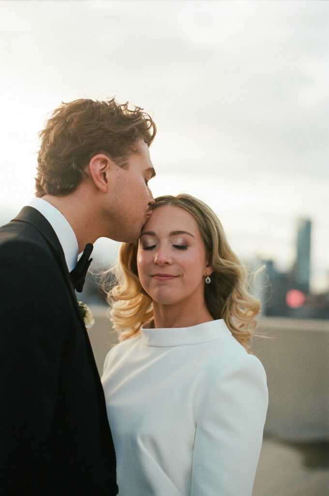 Film photograph of Boston groom kissing his bride at sunset