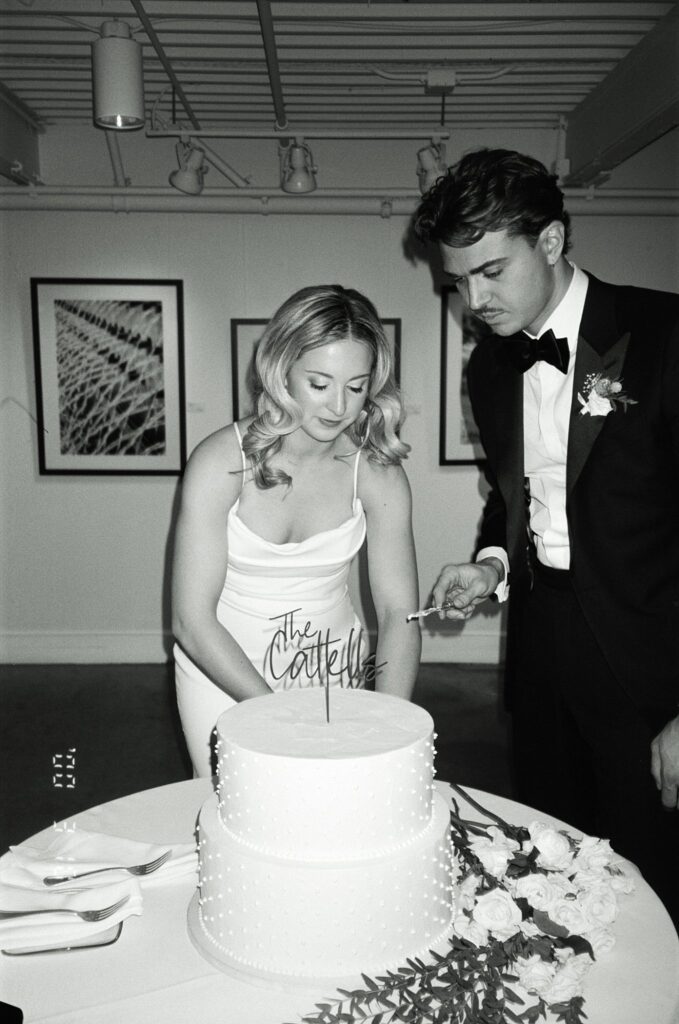 Boston bride cuts cake while groom looks on, in black and white