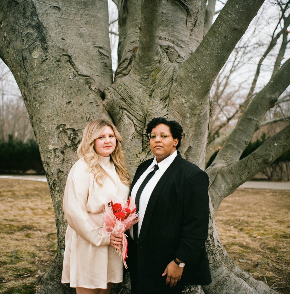 Boston brides stand before a large tree holding a wedding bouquet