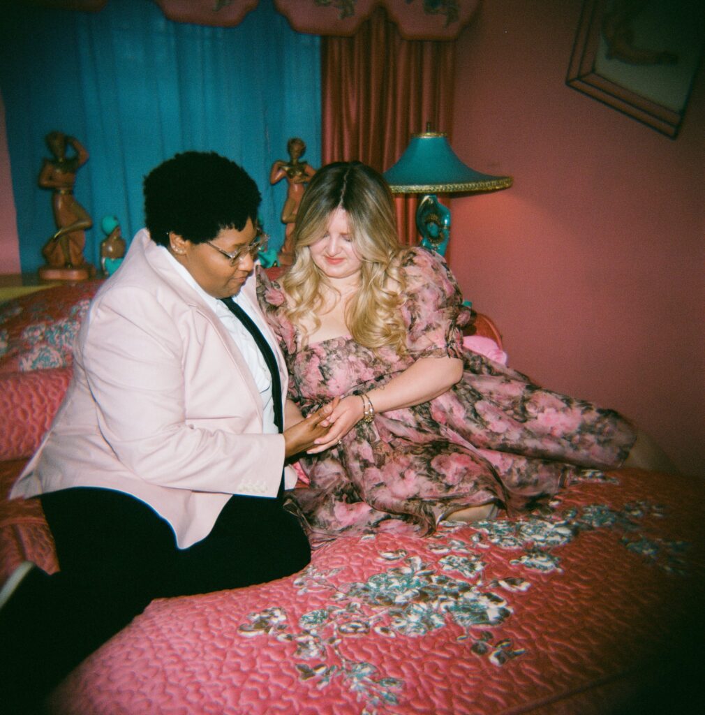 Two brides hold hands on a bed in a vintage inspired room