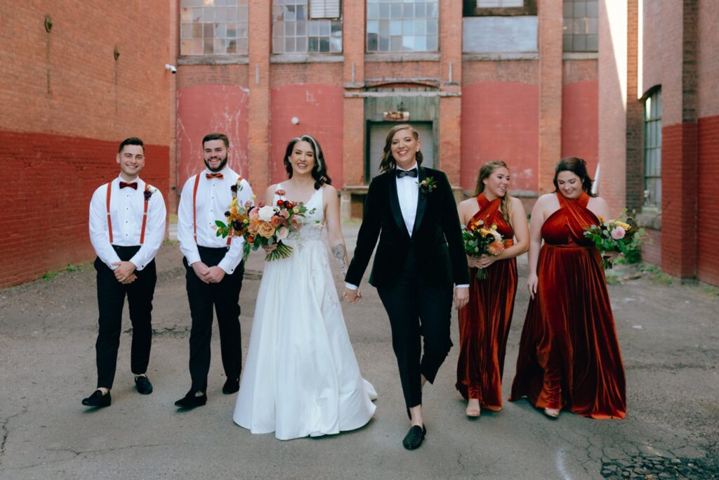 two brides walk and laugh with their wedding  party
