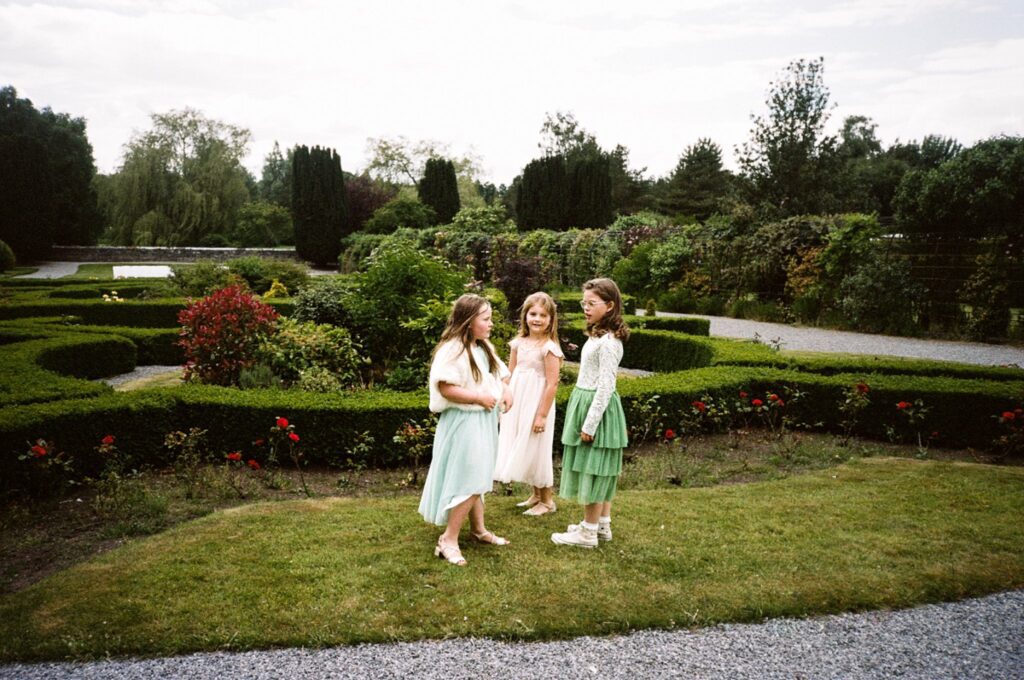 three young wedding guests stand in a garden
