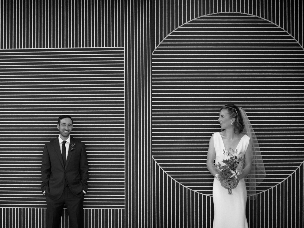 Black and white photograph of bride and groom posed in front of dramatic line art
