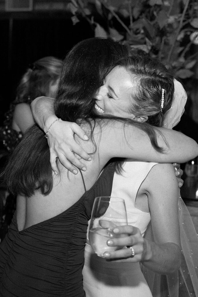 Bride embraces a wedding guest, in black and white film