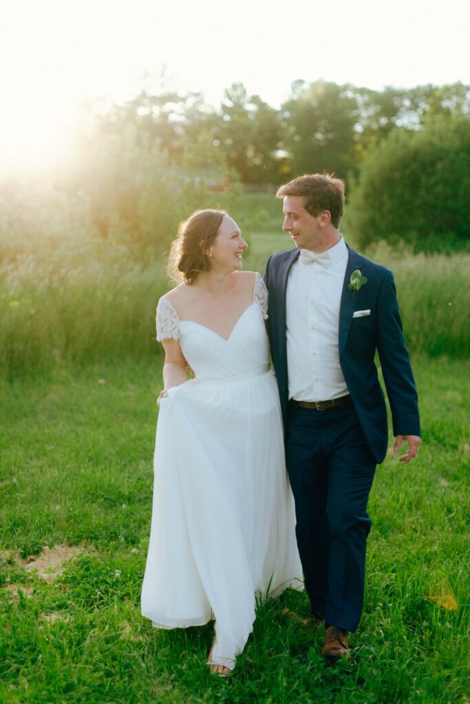 a bride and groom walk through a field at sunset