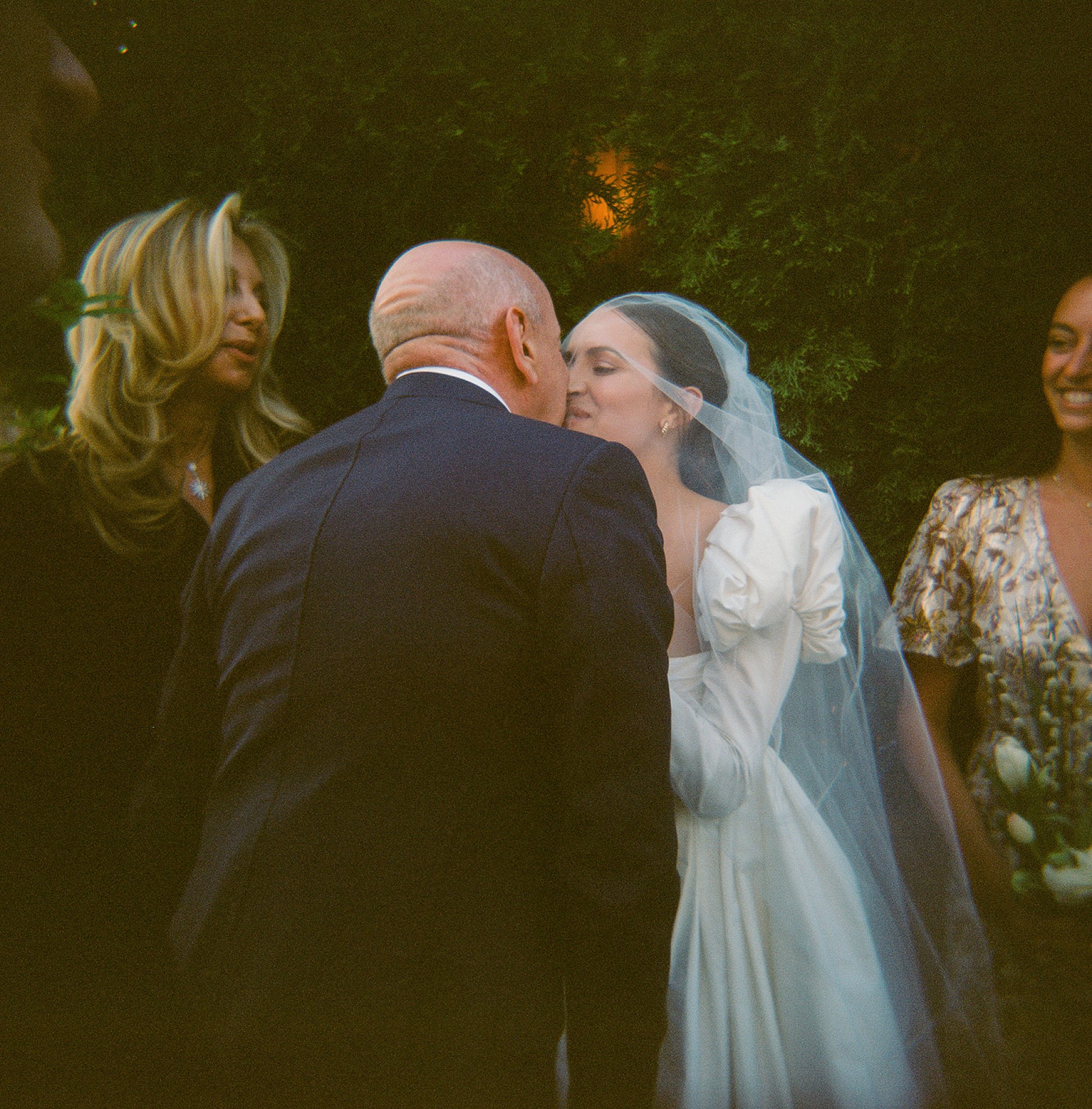 The bride and groom share a kiss as officiant and guests look on and smile.
