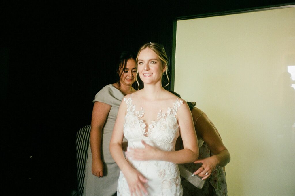 Film photo of bride smiling as she dons her dress