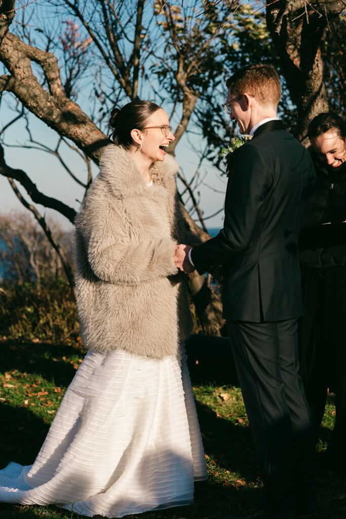 Bride in fur coat laughs at her ceremony, shot by Perth wedding photographer